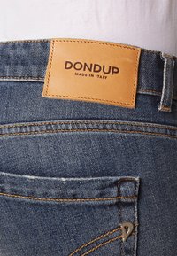 Jeans de mezclilla con un lavado azul oscuro, que presentan un parche de cuero etiquetado "DON DUP MADE IN ITALY" y costuras en contraste a lo largo de los bolsillos.