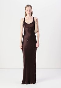 Hnedá saténová maxi šaty s priliehavým strihom, dekoltom do U a tenkými ramienkami. Zobrazené na modeli na jednotnom pozadí.