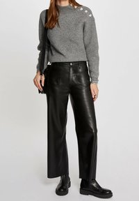 Harmaa ribbattu villapaita, jossa on pyöreä kaula-aukko ja metalliset yksityiskohdat olkapäissä, yhdistettynä korkeavyötäröisiin mustiin nahkahousuihin, joissa on leveä lahje.