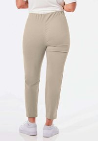 Beige joggingbroek met elastische taille, smal toelopende pijpen, een gladde textuur en een enkel-lengte snit, gecombineerd met witte sportschoenen.