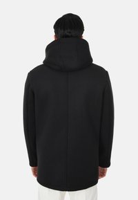 Cappotto nero con colletto alto e spalle strutturate, caratterizzato da una texture liscia e linee pulite, visto da dietro.