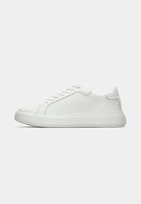 White sneaker featuring a textured leather upper with a repetitive logo pattern, round toe, and rubber sole with a subtle height increase.