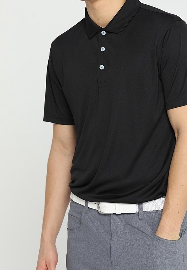 Mies, jolla on musta lyhythihainen poolopaita, harmaat housut ja valkoinen vyö, käsi taskussa.