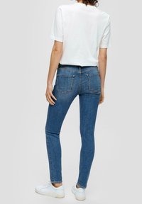 Jeans blu slim con design a cinque tasche, realizzati in denim. Abbinati a una maglietta bianca e a sneakers bianche, che evidenziano una silhouette aderente.