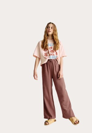 Lichtroze cropped T-shirt met een grafisch ontwerp, gecombineerd met losse bruine linnenbroek en beige slip-on sandalen.