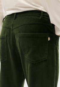 Grüne Cordhosen mit strukturierten Oberflächen, hinteren Taschen mit Klappen und einem kleinen Markenlogo in der Nähe des Taillenbundes.