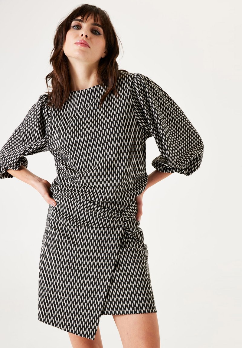 Un vestido de patrón en blanco y negro con una tela texturizada, que presenta mangas abullonadas y un diseño de envoltura asimétrica.