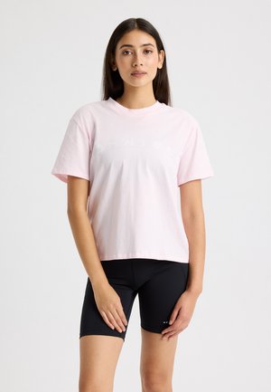 Lyserød bomulds t-shirt med rund hals og korte ærmer, prydet med hvid tekst i en buet design. Sammen med sorte cykelshorts.