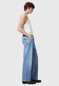 Jeans largi de culoare deschisă, din denim, cu un design clasic cu cinci buzunare și o curea neagră, asortați cu un top alb fără mâneci.