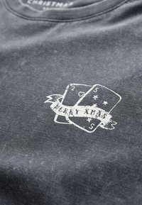 Dark gray T-shirt featuring a distressed white print of playing cards with "MERRY XMAS" on a banner. Cotton material with a crew neck.