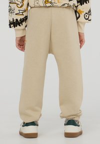 Beżowe dresy z elastycznymi mankietami, wykonane z miękkiego materiału. Charakteryzują się luźnym krojem. Połączone z białymi i zielonymi sneakersami.