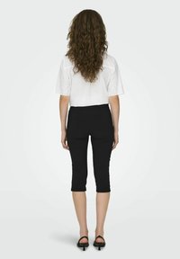 Blouse blanche en dentelle avec des manches courtes, associée à un pantalon noir court, présentant une silhouette ajustée. Porté avec des sandales noires.