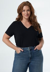 T-shirt noir à col en V avec des manches courtes, porté rentré dans un jean en denim bleu taille haute ; présente une coupe décontractée et une texture de tissu lisse.