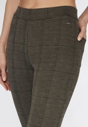 Nahaufnahme der Taille und Hüften einer Person, die braune karierte Hose mit tailliertem Bund und dezentem Seitenfach trägt, Hand ruht nahe der Tasche.