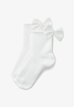 Białe skarpetki do kostek z dużymi kokardami wykonanymi z tkaniny przyszytymi blisko górnej krawędzi, prezentowane na płasko na białym tle.