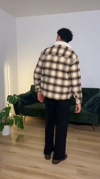 Geruit flanellen overhemd in beige, bruin en wit tinten; voorzien van een overhemdkraag, knoopmanchetten en een losse pasvorm. Draagt bij zwarte broek.