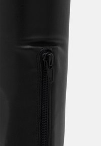 Bota de cuero sintético negro con una textura suave, que presenta un detalle de cremallera lateral y una silueta ajustada.