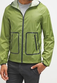 Green mesh jacket with a zip front, two zippered pockets, and a hood. Features navy blue accents along the pocket edges and cuffs.