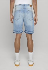 Svetlo modré rifle s raw lemom, vyblednutým dizajnom, dvoma zadnými vreckami a hnedou visačkou na páse. Biely tenisky s gumovými podrážkami.