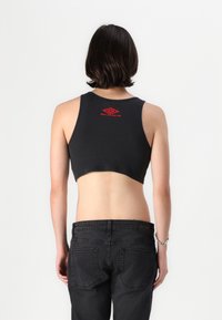 Black ribbed cropped tank top with red logo detail at the back, paired with black jeans. Smooth texture, fitted design, and sleeveless.