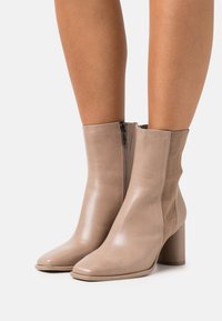 Bottines beiges avec une finition en cuir lisse, un bout carré, des panneaux élastiques latéraux et un talon bloc solide. Fermeture à glissière sur un côté.
