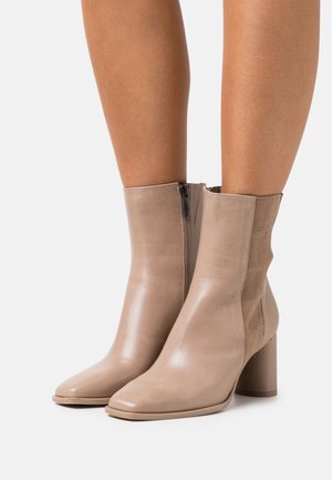 Beige ankle boots with a smooth leather finish, a square toe, side elastic panels, and a sturdy block heel. Zipper closure on one side.