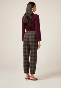 Bordeaux gebreide trui, losse pasvorm, gecombineerd met geruite broek in donkere tinten, met een elastische tailleband en taps toelopende enkels. Schoenen met een lage hak.