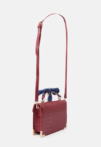 Czerwona torebka crossbody z tłoczonej skóry krokodyla z złotym akcentem w narożnikach i niebieskim szalem zawiązanym na uchwycie. W zestawie regulowany pasek.