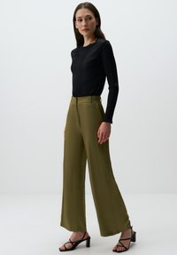 Czarny prążkowany top z długim rękawem w połączeniu z oliwkowymi spodniami typu wide-leg z wysokim stanem, charakteryzującymi się gładką fakturą i akcentami w postaci klamer. Czarne sandały na obcasie z paskami.