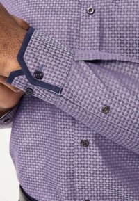 Paarse gestreepte shirt met een geometrisch ontwerp, contrasterende blauwe accenten op de manchetten en donkere knopen voor extra detail.