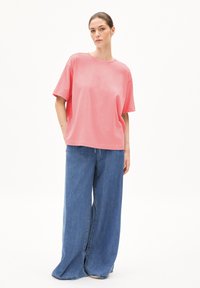 Lichtroze katoenen T-shirt met een losse pasvorm, korte mouwen en een ronde halslijn, gecombineerd met blauwe denim jeans met wijde pijpen.