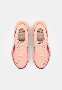 Nike running shoes in coral with a textured mesh upper. Features a black swoosh and purple accents on the sole. Laces are flat and pink.