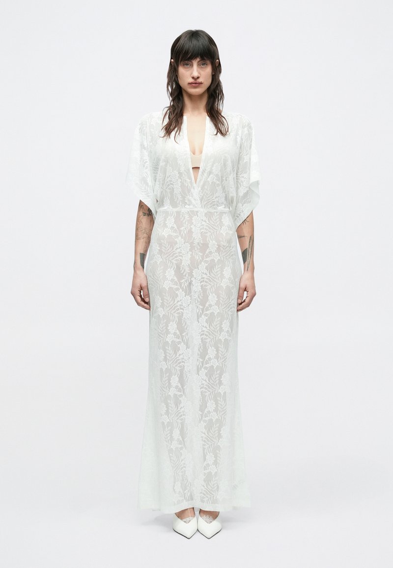 Pikk, läbipaistev valge kimooni kleit, millel on lillelised pitsmustrid ja sügav V-kaelus. Varrukad on laiad ja voolavad, talje on liibuv.