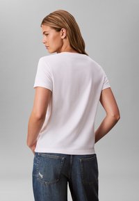 T-shirt bianca in cotone a maniche corte con scollo rotondo, design semplice e vestibilità comoda, abbinata a jeans di denim blu con tasche posteriori.