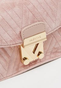 Borsa a tracolla in suede rosa con texture trapuntata, chiusura in metallo dorato con un design geometrico e dettagli del logo impressi sul flap.