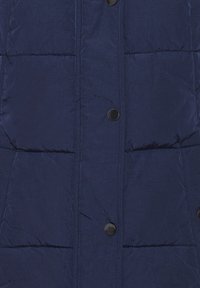 Marinblå pufferväst gjord av slätt, lätt material. Har horisontella quiltade sektioner och svarta tryckknappar framtill.