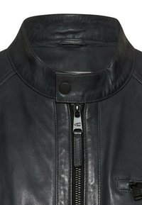 Kołnierz czarnej skórzanej kurtki z zatrzaskiem i srebrnym suwakiem, pokazujący szczegóły z bliska oraz fakturę materiału.