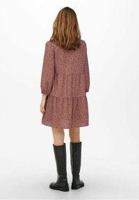 Vestido rojo con estampado, mangas abullonadas, diseño en capas y de longitud hasta la rodilla. Combinado con botas negras hasta la rodilla de cuero suave.