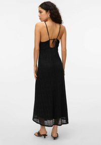 Robe maxi en crochet noir avec des bretelles spaghetti, détail au dos ouvert et fermeture à nouer. Ourlet évasé avec des motifs complexes tout au long.