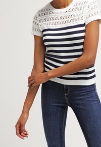 Top de punto a rayas azul marino y blanco con canesú de encaje. Mangas cortas y diseño ajustado, con un patrón de encaje abierto y texturizado en los hombros.