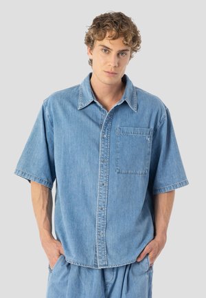 Vaaleansininen denimpaita, jossa on lyhyet hihat, terävä kaulus, etutasku ja napillinen edessä, rento istuvuus ja sileä pinta.