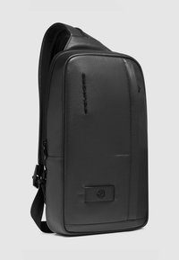 Zwarte leren rugzak met een gladde afwerking, rechthoekige vorm, zijrits en een voorvak met een merkaccent. Inclusief verstelbare riem.