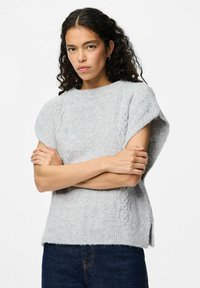 Ljusgrå kabelstickad tröja med korta ärmar, ribbad halsringning och sidofack. Mjuk textur, avslappnad passform, matchad med mörka jeans.