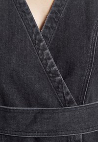 Gros plan sur un vêtement en denim noir délavé avec un col en V et une ceinture large enroulée autour de la taille.