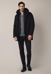 Czarna pikowana parka z kapturem, nałożona na szaro-splątany sweter. Slim fit czarne dżinsy i czarne skórzane botki za kostkę dopełniają strój.