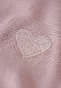 Rosa gestrickter Stoff mit einem gestickten herzförmigen Patch in einem leicht helleren Rosa.