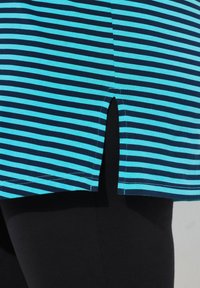 Top a rayas azul y marino con una abertura lateral, hecho de una tela suave, combinado con leggings negros. Se pueden ver detalles de costura limpios.