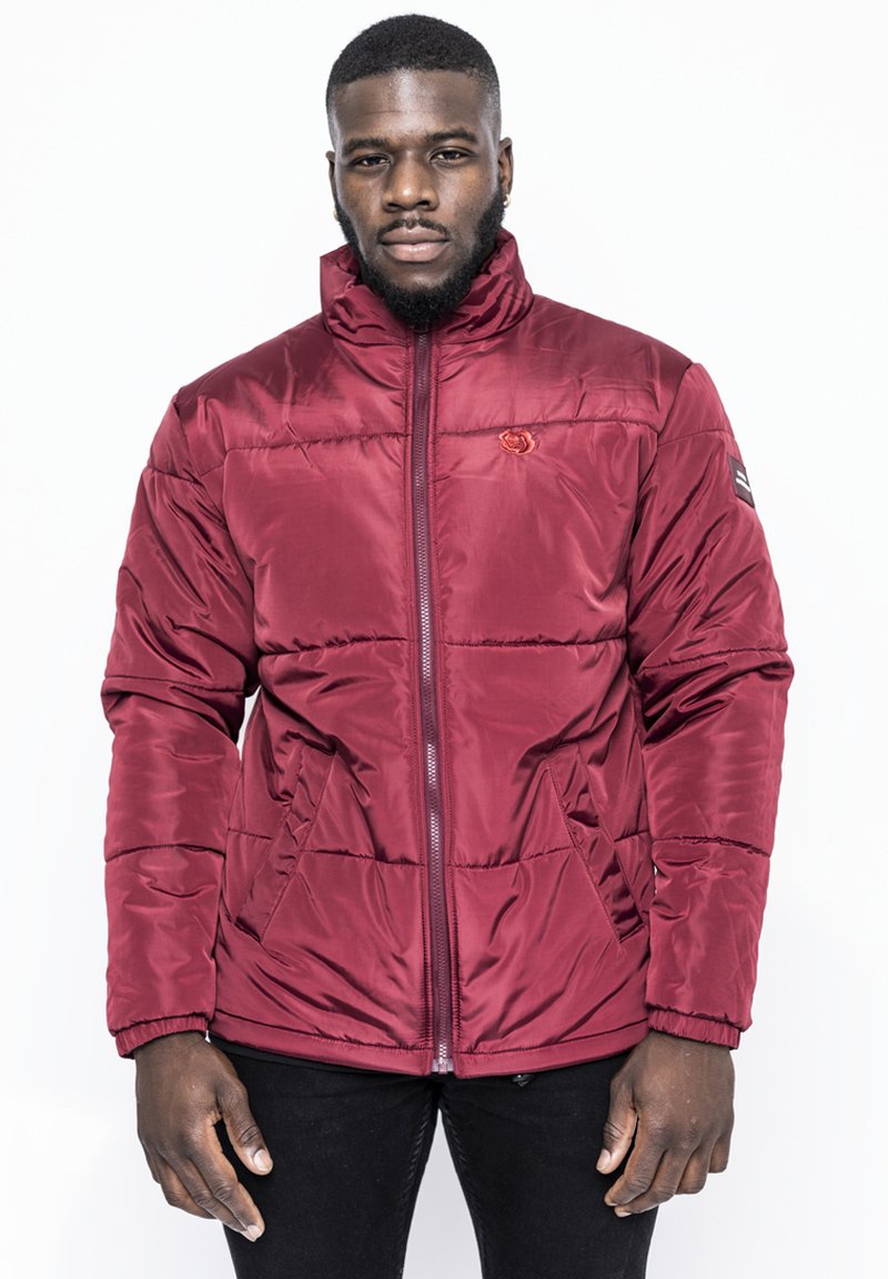 Giacca a vento bordeaux con chiusura a zip, colletto alto e due tasche laterali. Presenta cuciture diagonali e un piccolo logo sul petto.