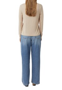 Beige langärmliges Oberteil kombiniert mit lockeren, hellblauen Denim-Jeans, die einen geraden Schnitt und Gesäßtaschen aufweisen. Weicher Stoff, bequemer Sitz.