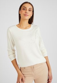 Ivoor gebreide trui met een ronde halslijn en lange mouwen, met een patroon van kleine, glinsterende rhinestones aan één kant.